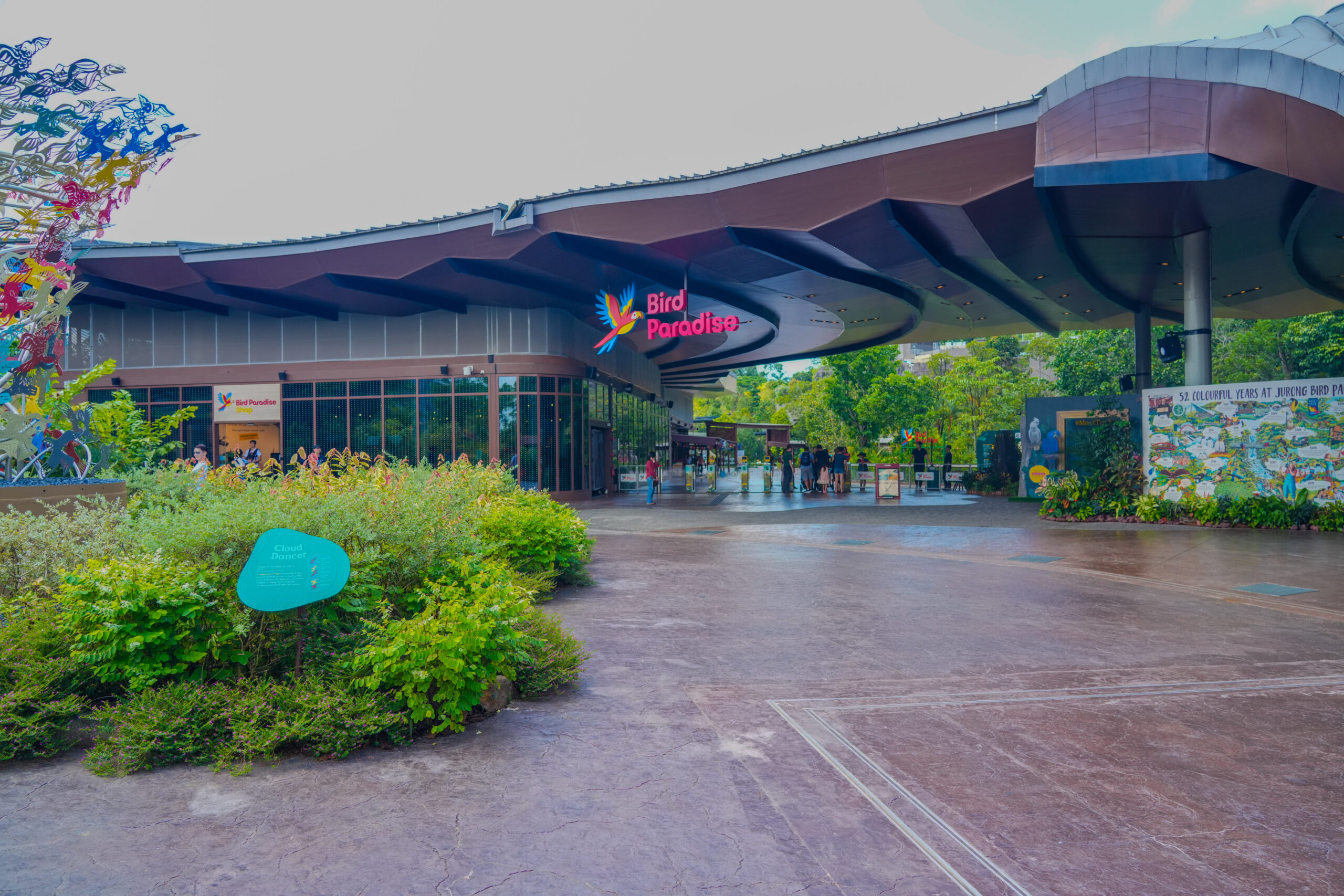 Entrance of Bird Paradise Singapore with a modern canopy, lush greenery, and visitors at the entrance.