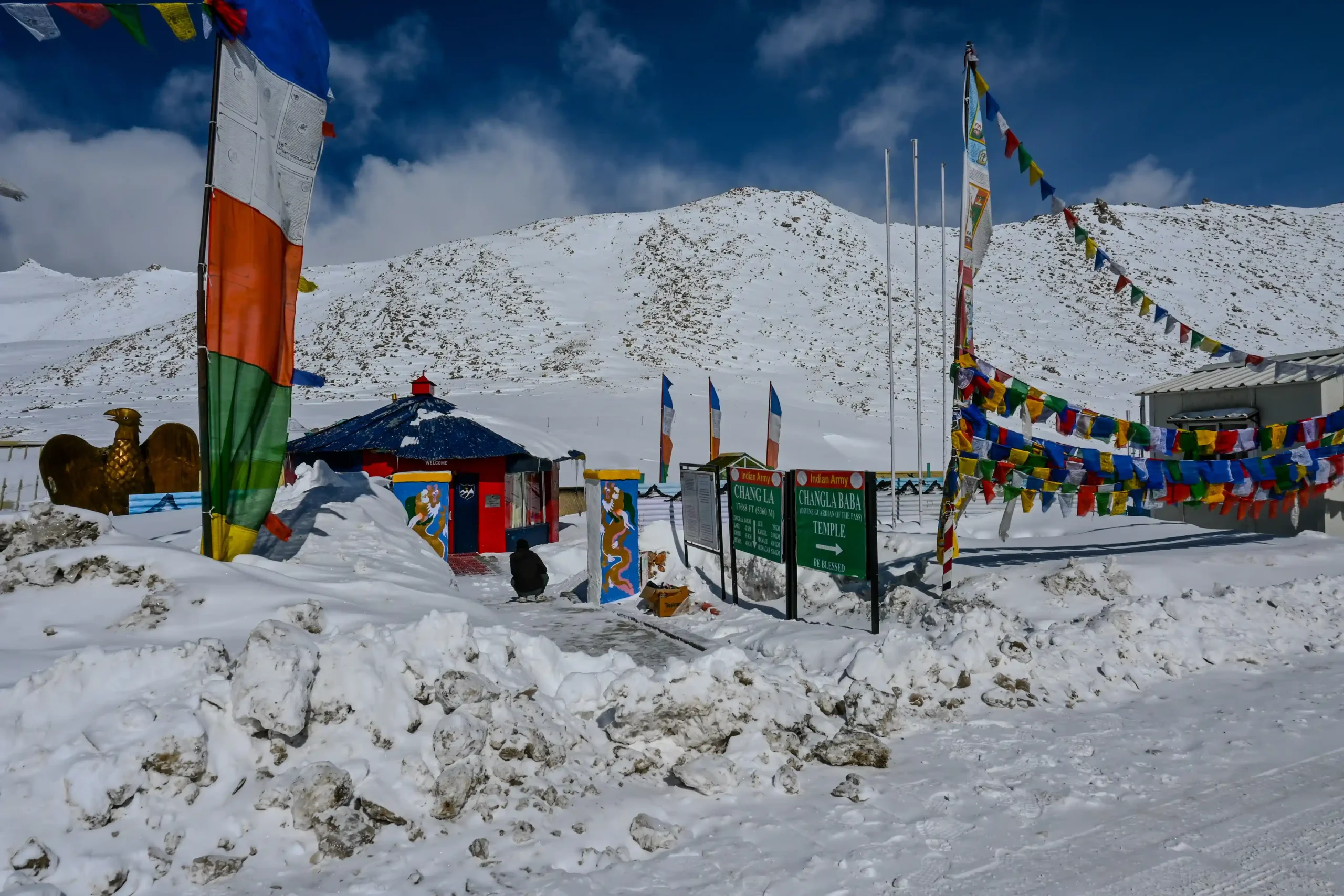 Frozen Chang La Pass with roadside signs and colorful prayer flags fluttering in heavy winter snow, Leh, Ladakh.