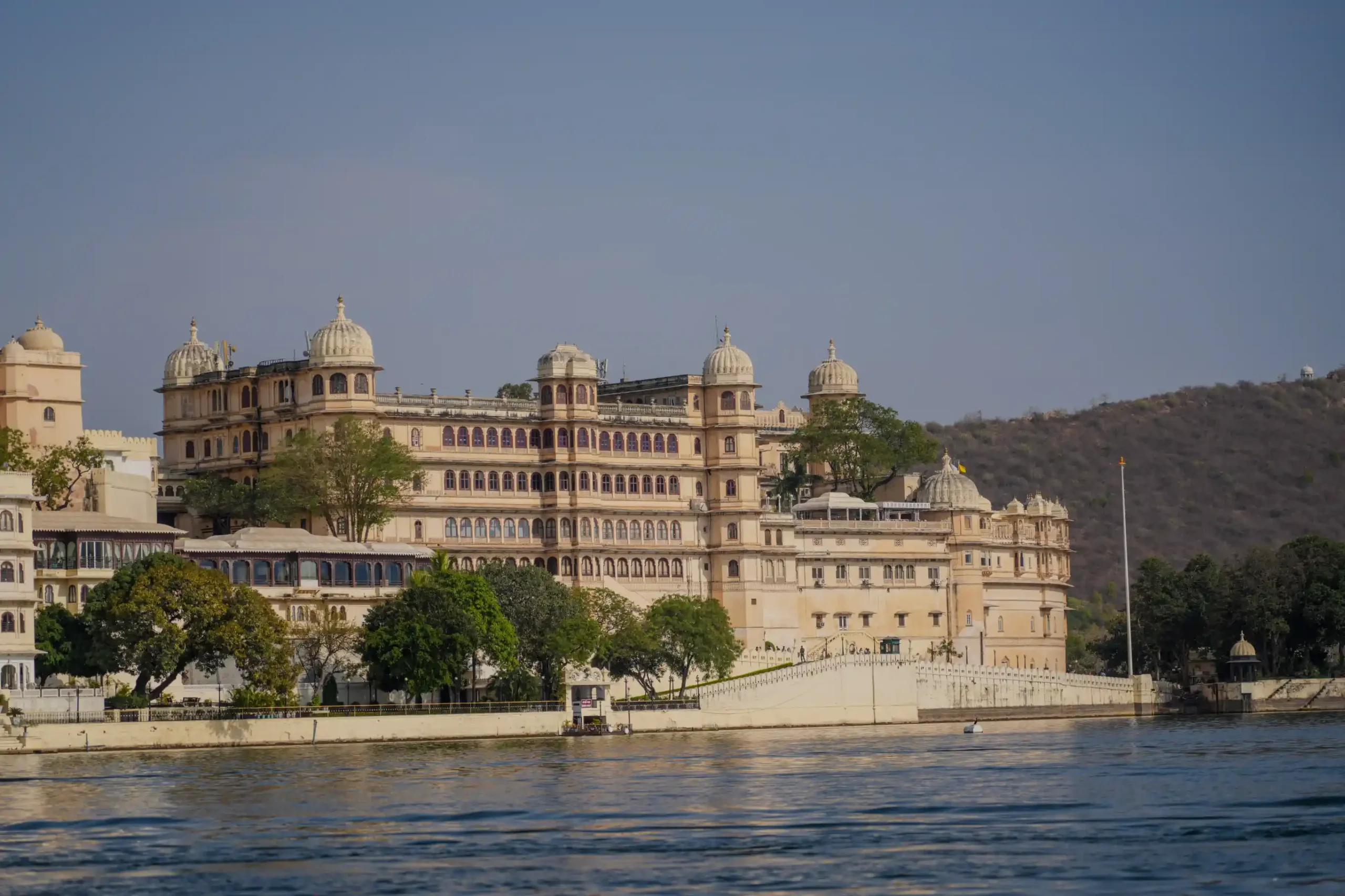 City Palace Udaipur seen from Lake Pichola with domes and arched facade against Aravalli hills