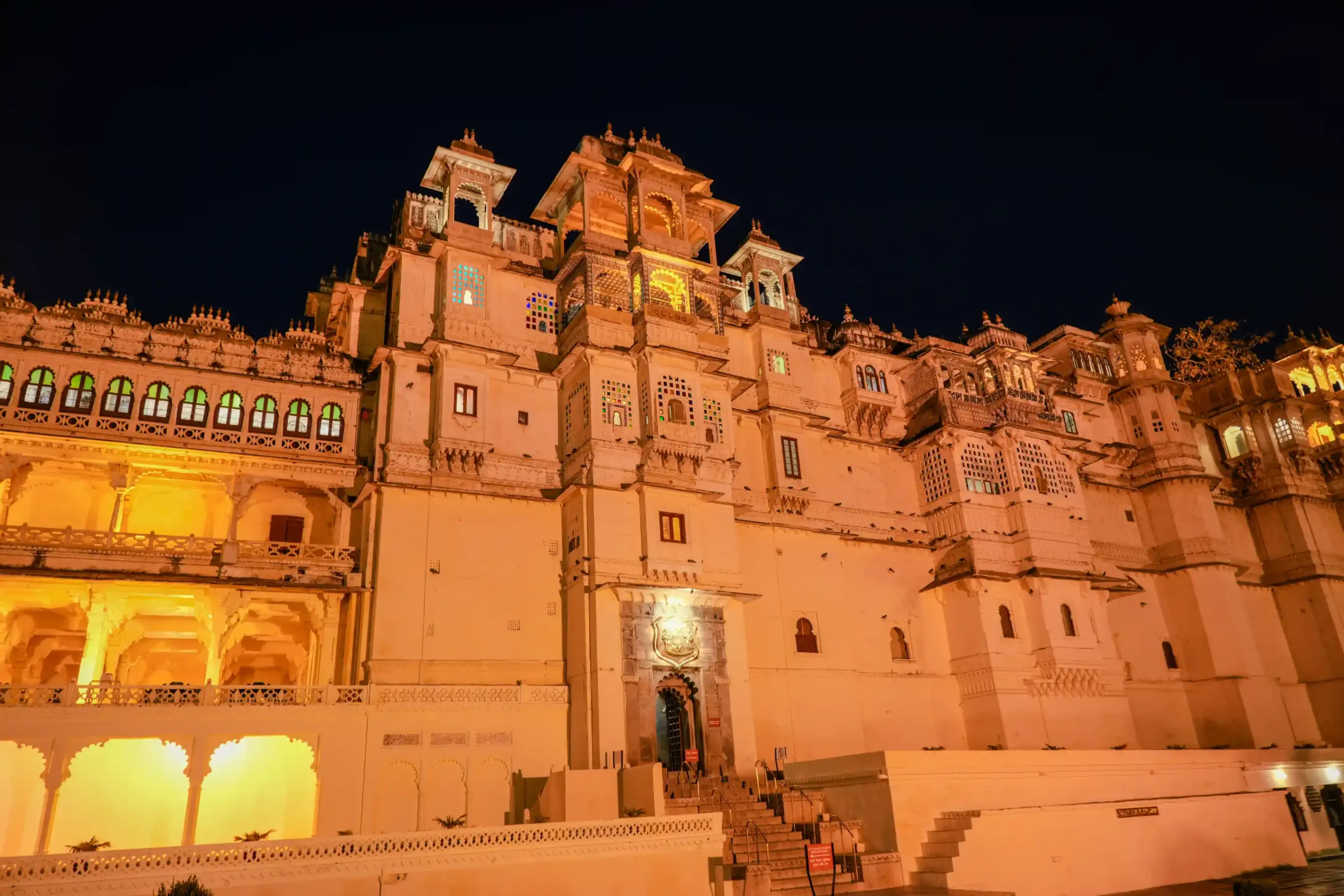 Night illumination of Udaipur City Palace facade with arched windows and jharokha balconies