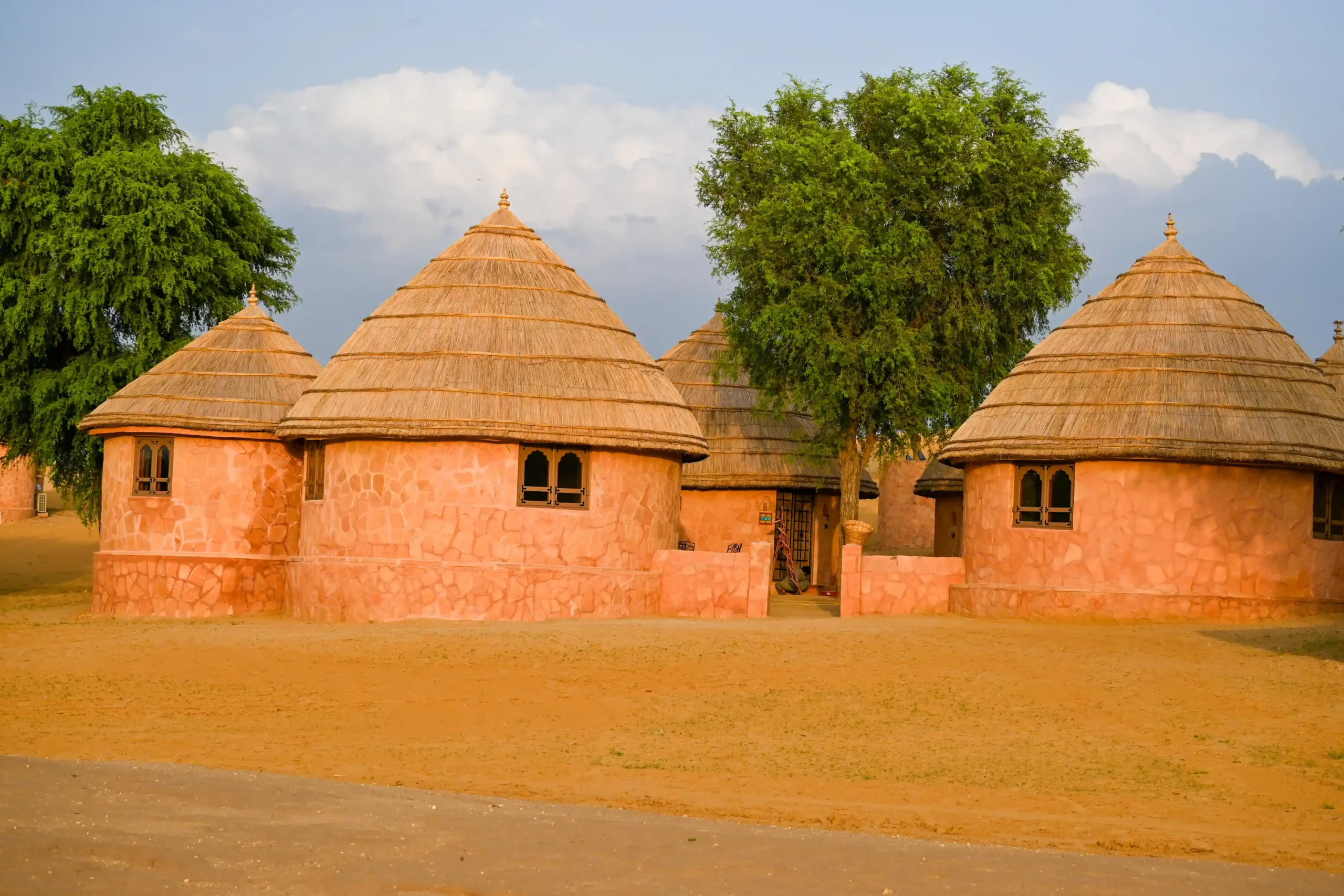 Front view of round thatched desert huts with pink stone walls at Khimsar Sand Dunes resort, Rajasthan