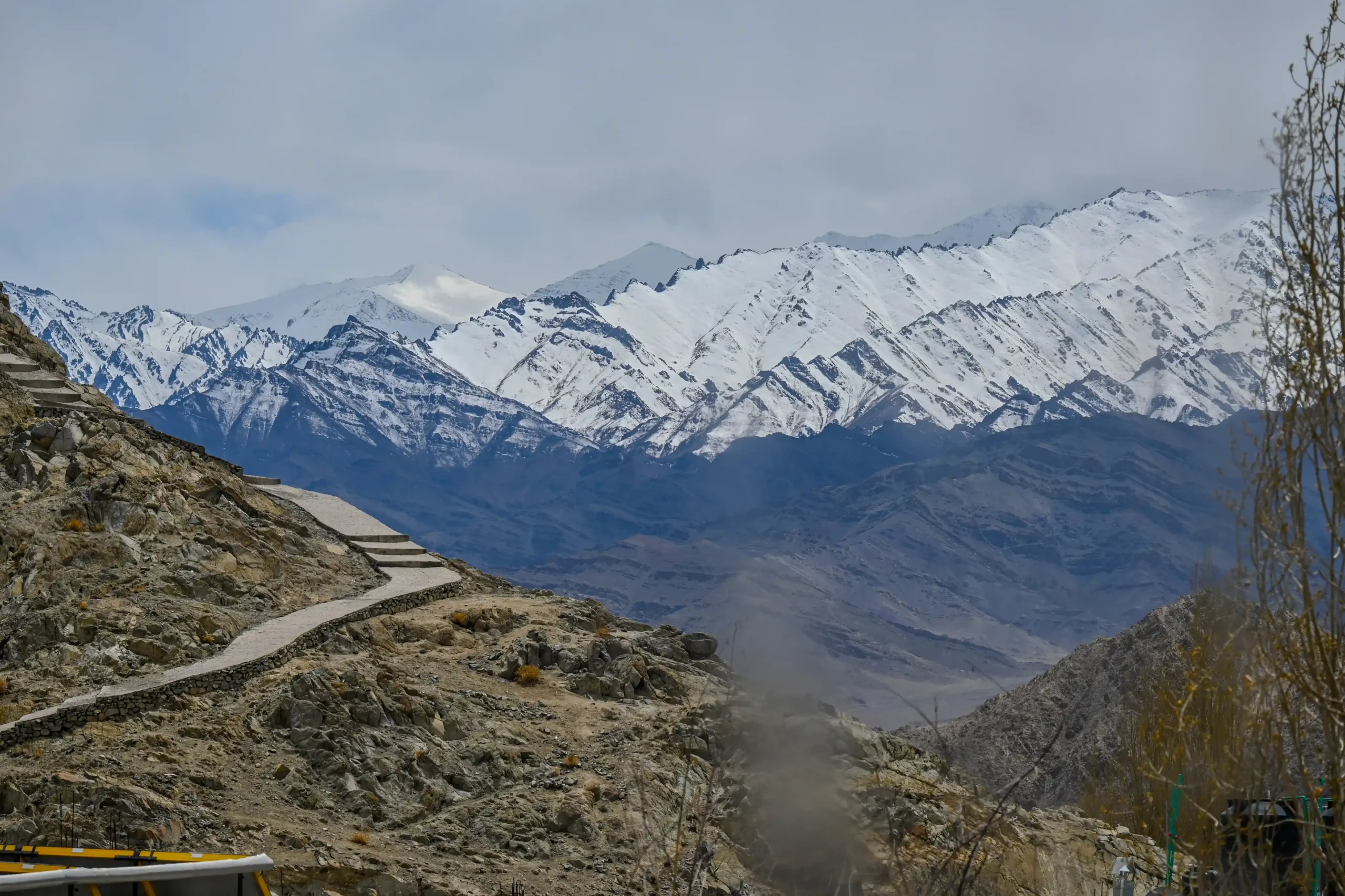 Snow-capped Himalayan mountains with rocky foothills under a pale winter sky in Leh, Ladakh.