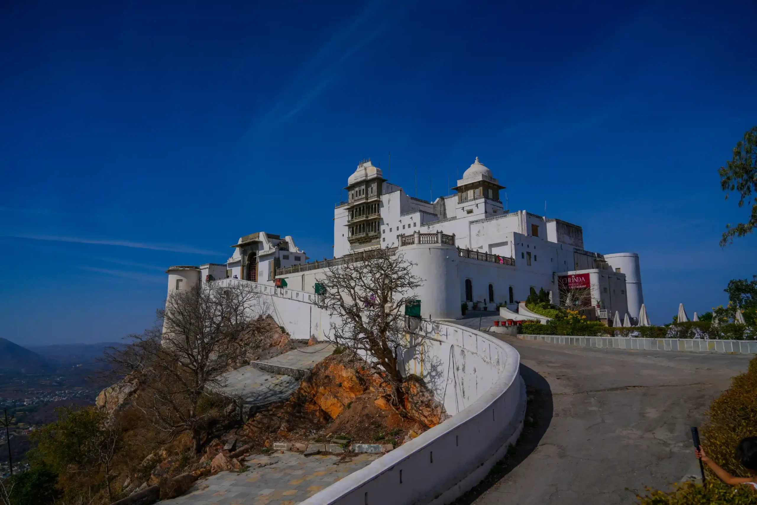 Monsoon Palace Udaipur perched on Sajjangarh hill with curving road under a deep blue sky