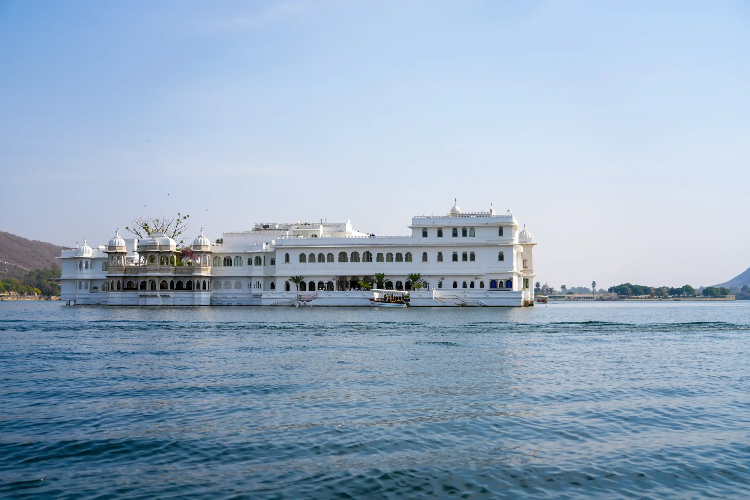 Taj Lake Palace viewed from a boat on Lake Pichola, Udaipur, with white marble facade and calm blue water