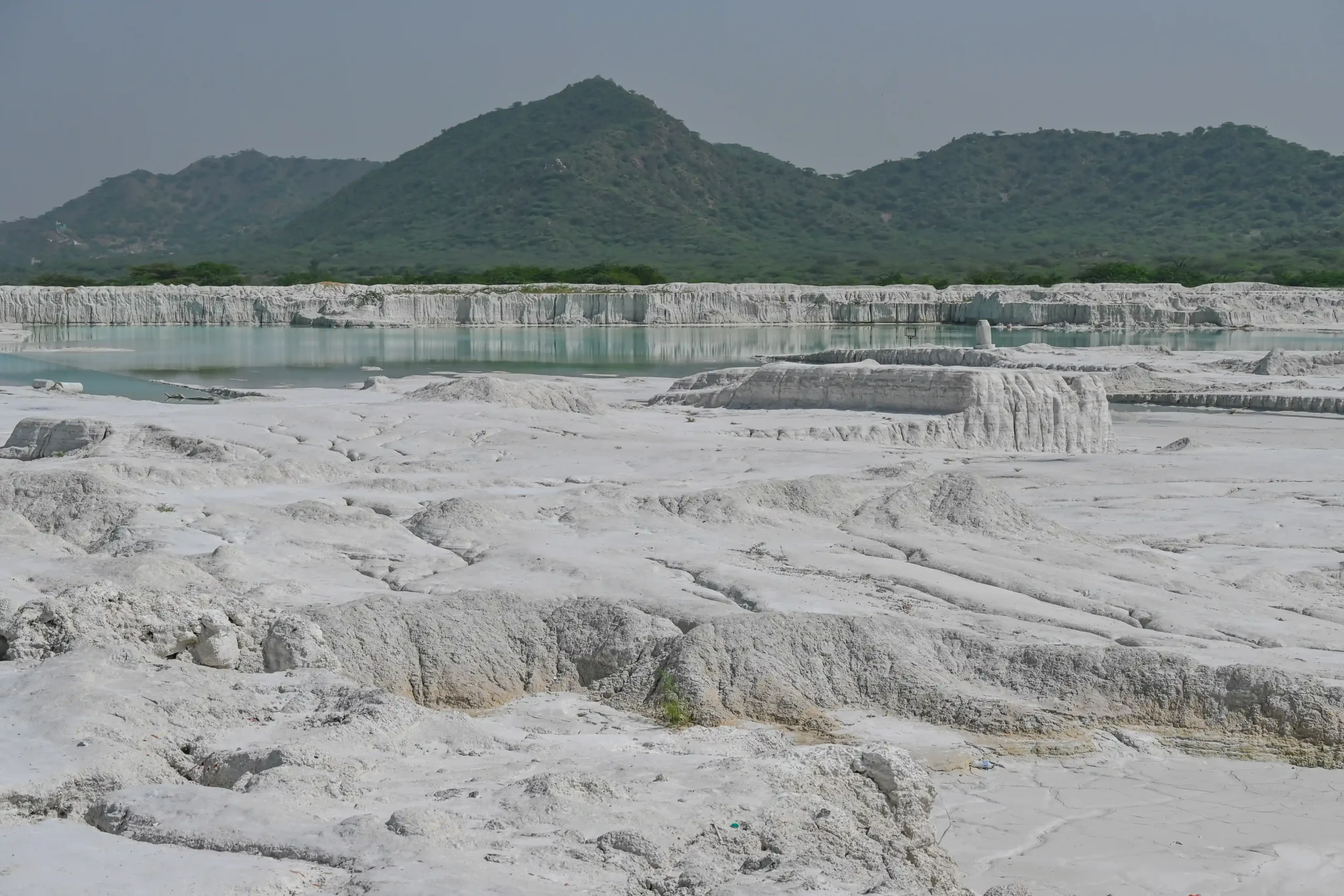 Textured white marble waste terrain with turquoise pool and Aravalli hill backdrop at Kishangarh, Rajasthan