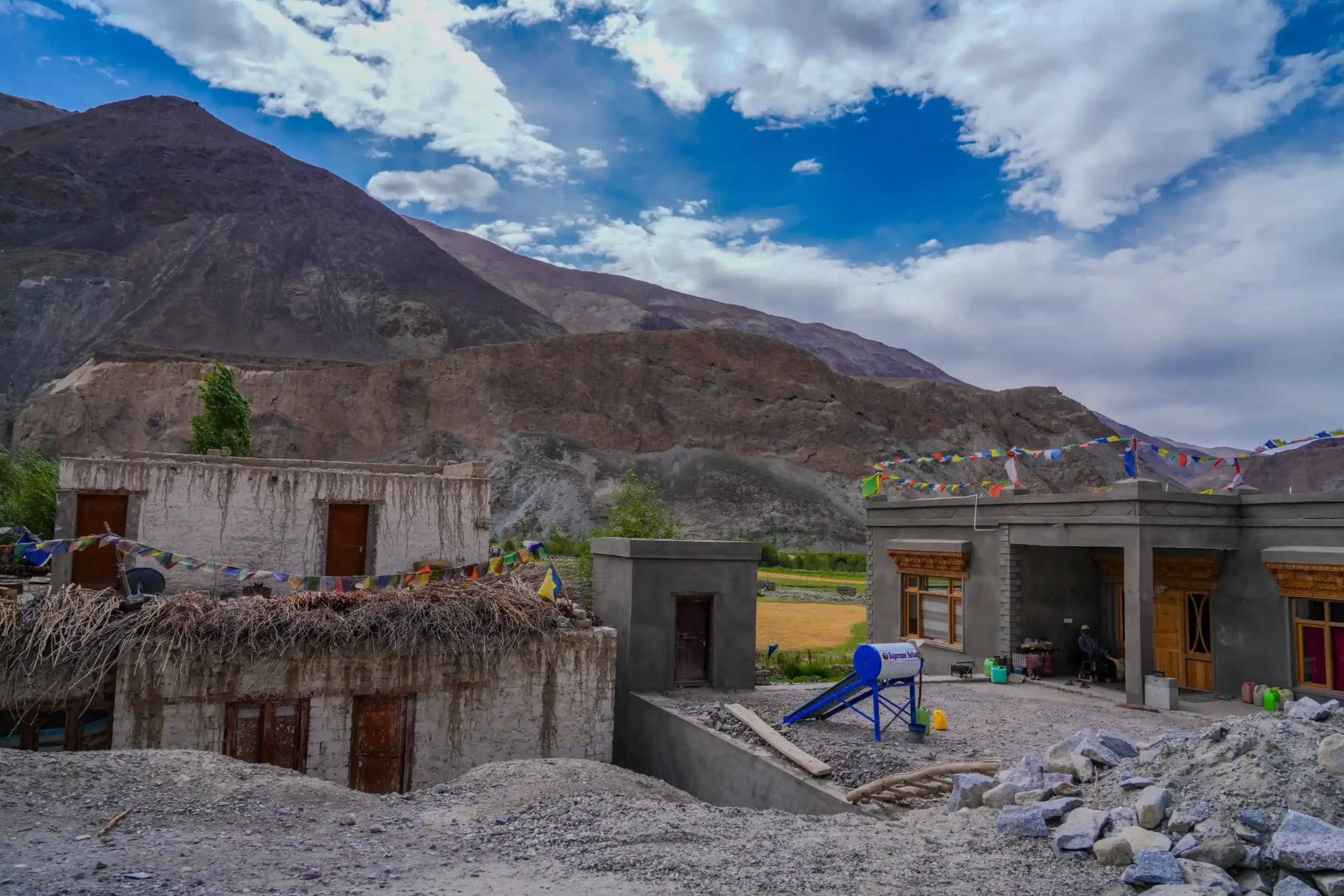 Traditional Ladakhi village homes with flat roofs and prayer flags, set against rocky mountains and a dramatic sky in Leh.