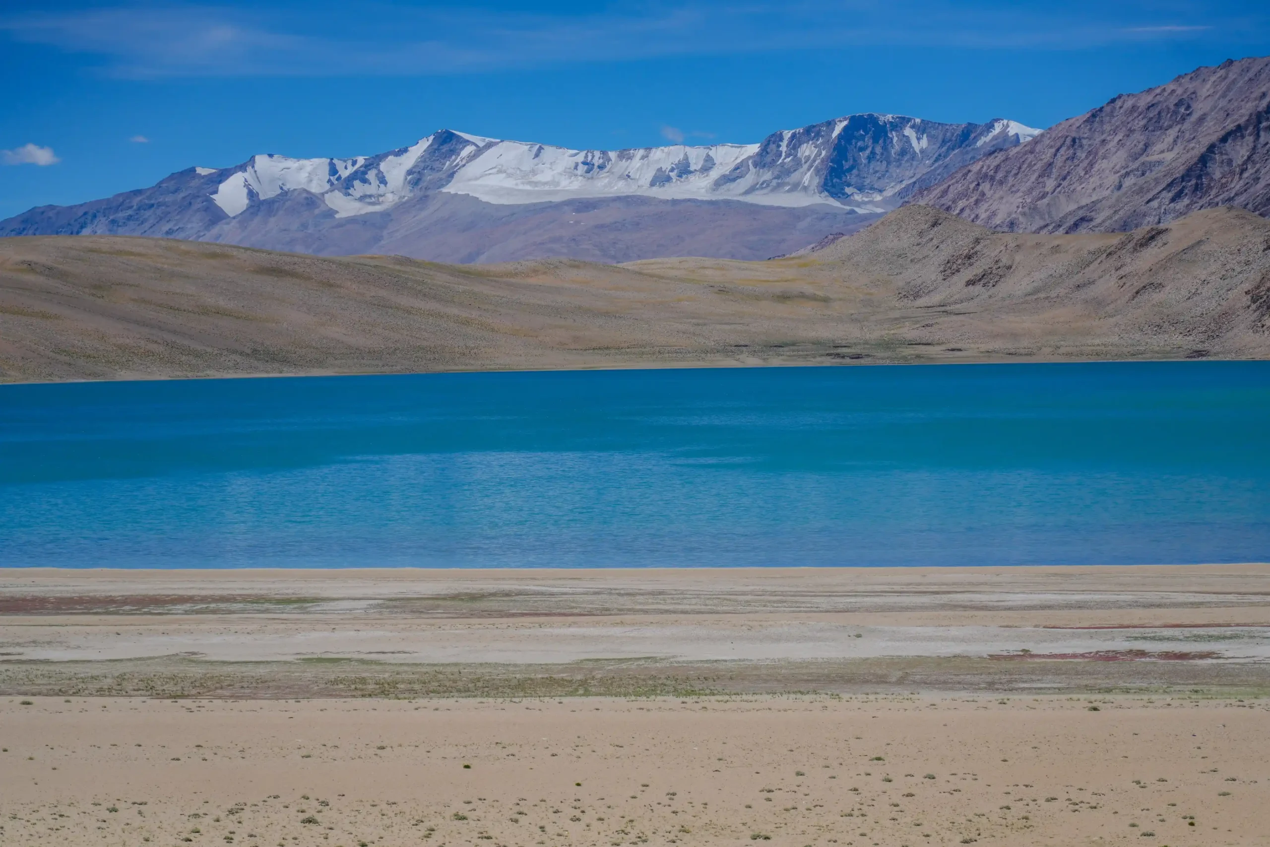 Tso Moriri Lake’s deep blue water surrounded by rolling barren hills and distant snow-capped mountains in Ladakh.