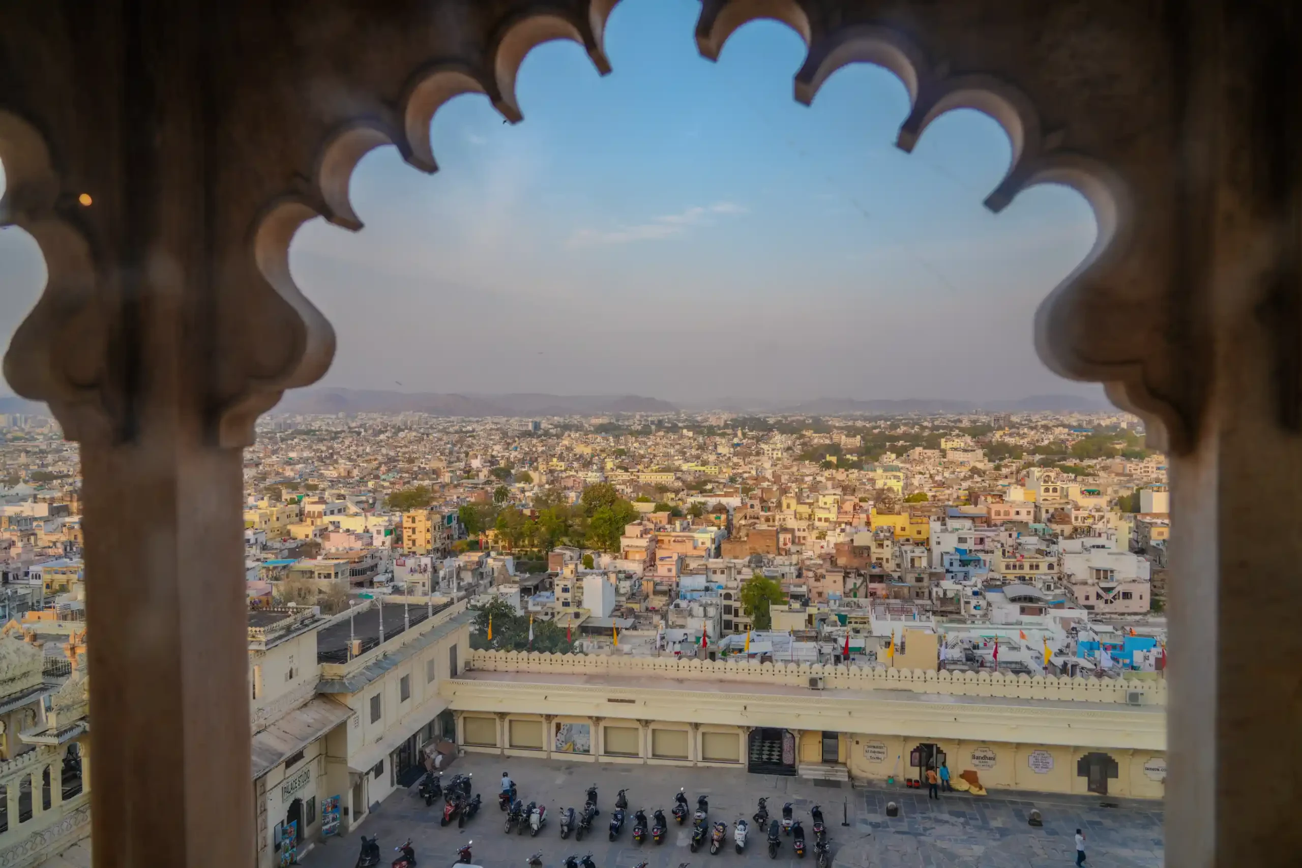 Panoramic Udaipur cityscape framed by ornate palace arch window at sunset