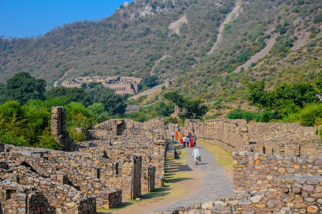 Wide view of Bhangarh Fort ruins in Alwar with a stone pathway, scattered structures, and Aravalli hills under a clear blue sky