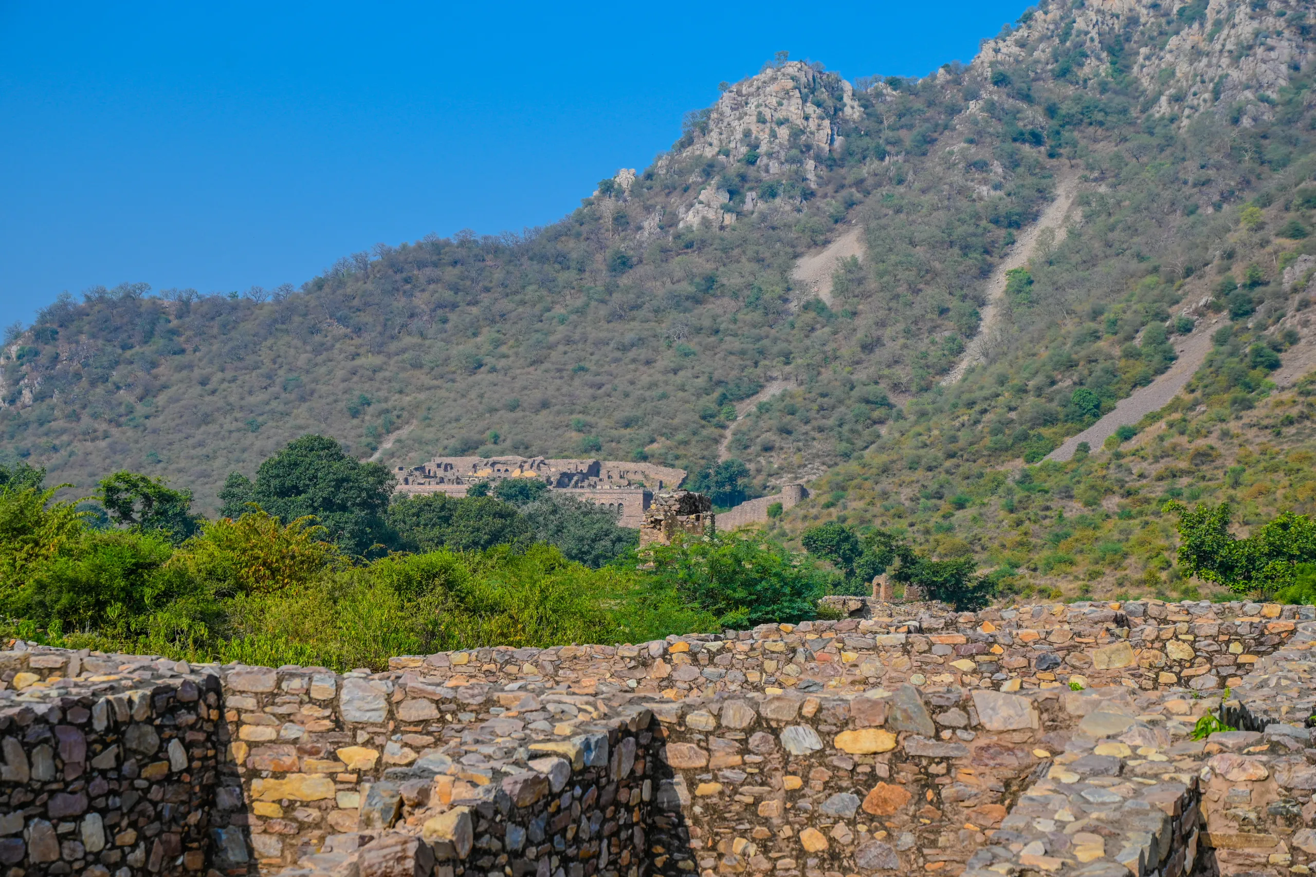 Old ruined tower at Bhangarh Fort with the Aravalli hillscape and a hilltop pavilion in the background