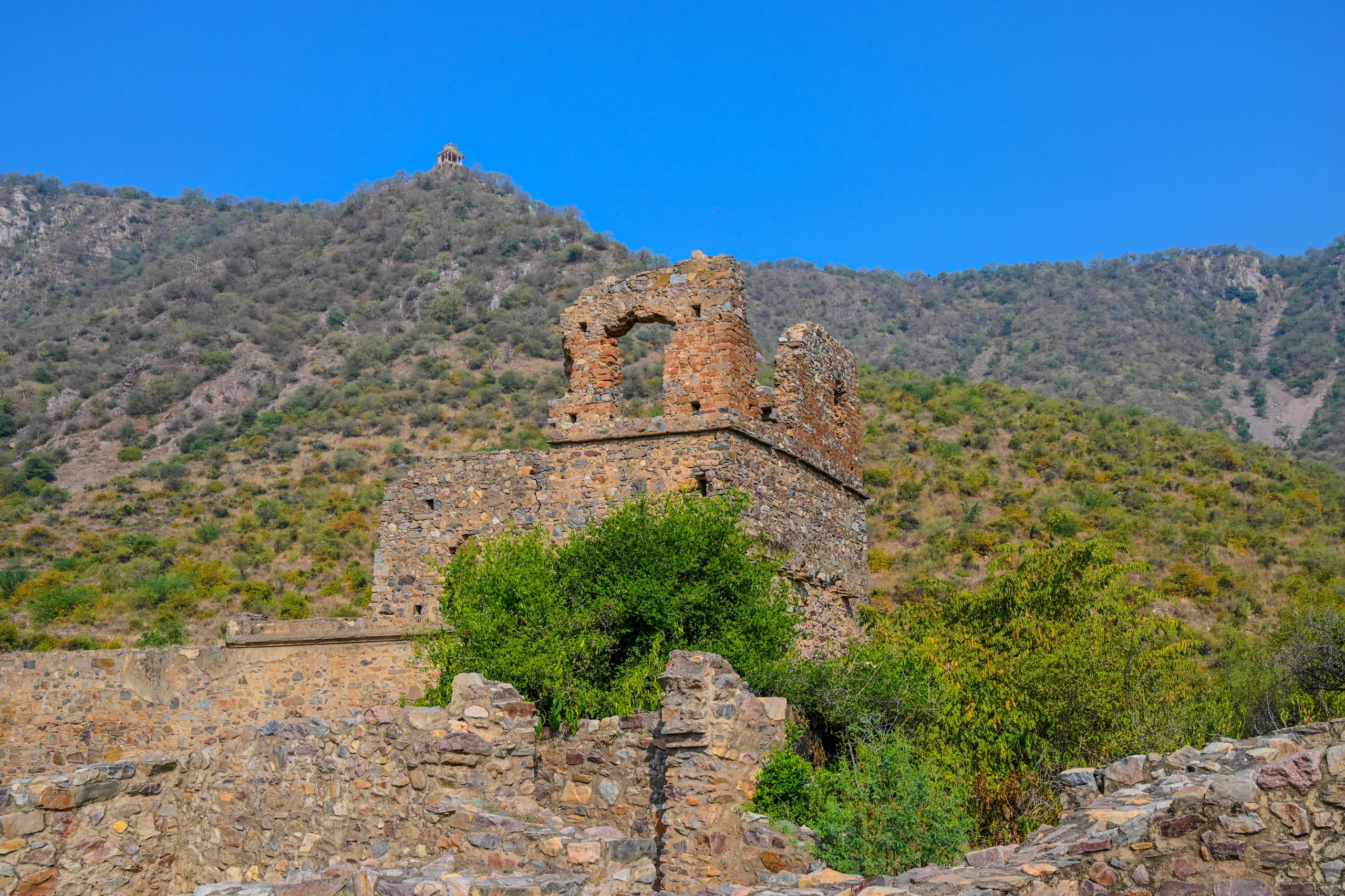 Stone ruins and broken arched walls at Bhangarh Fort with the Aravalli hills in the background