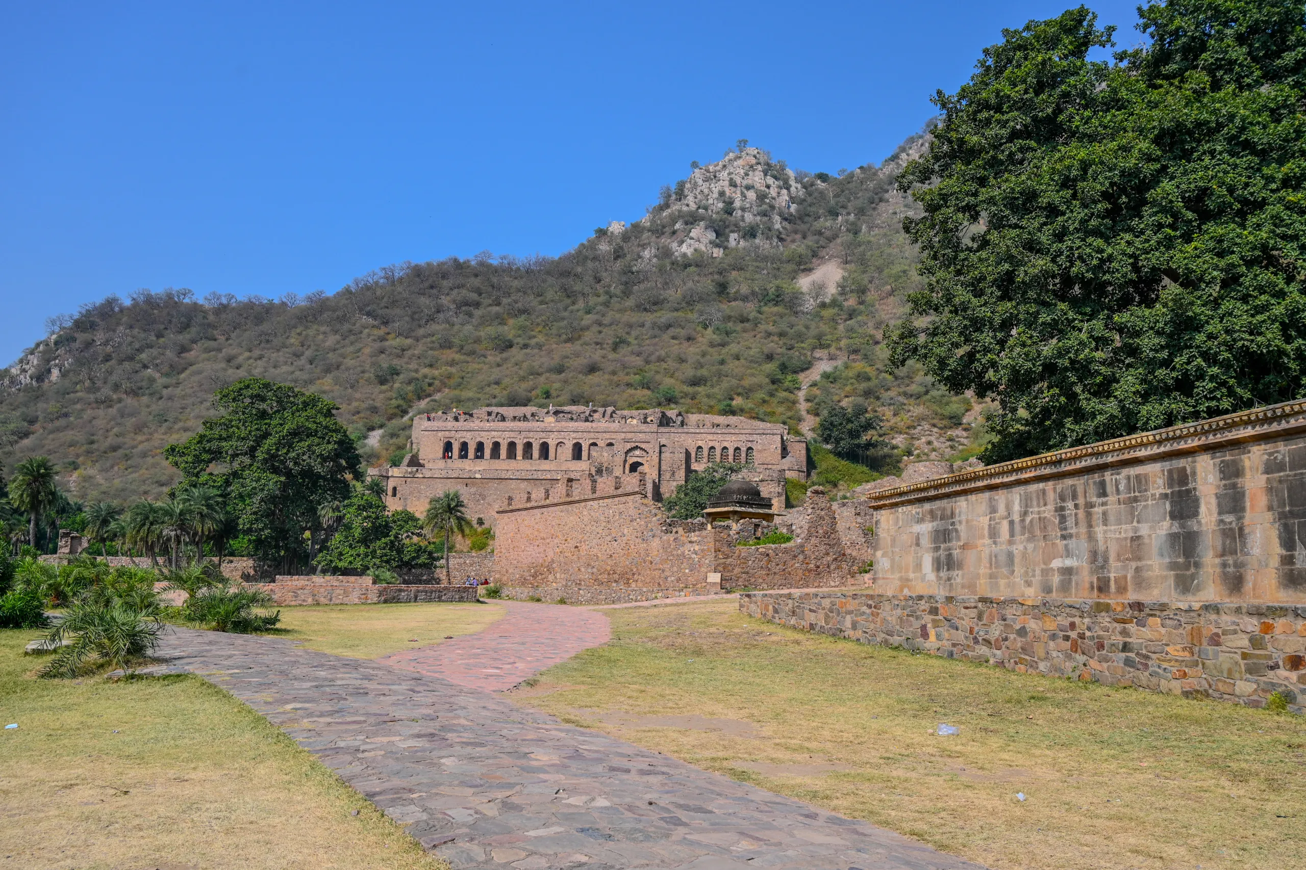 Historic stone ruins of Bhangarh Fort with a hillside structure and dry vegetation in Rajasthan