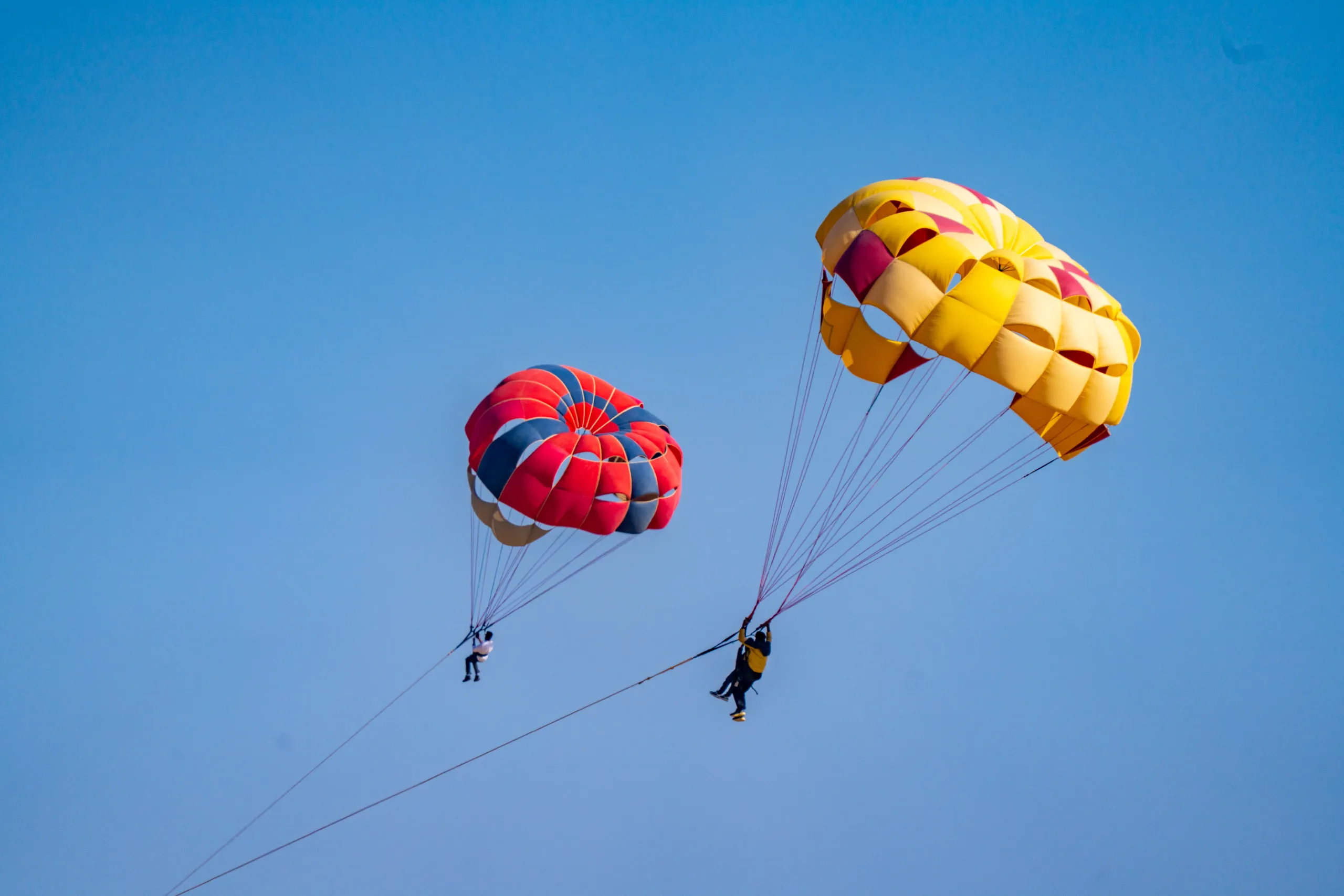 Two colorful parasailing canopies floating above Sam Sand Dunes near Jaisalmer against a blue sky