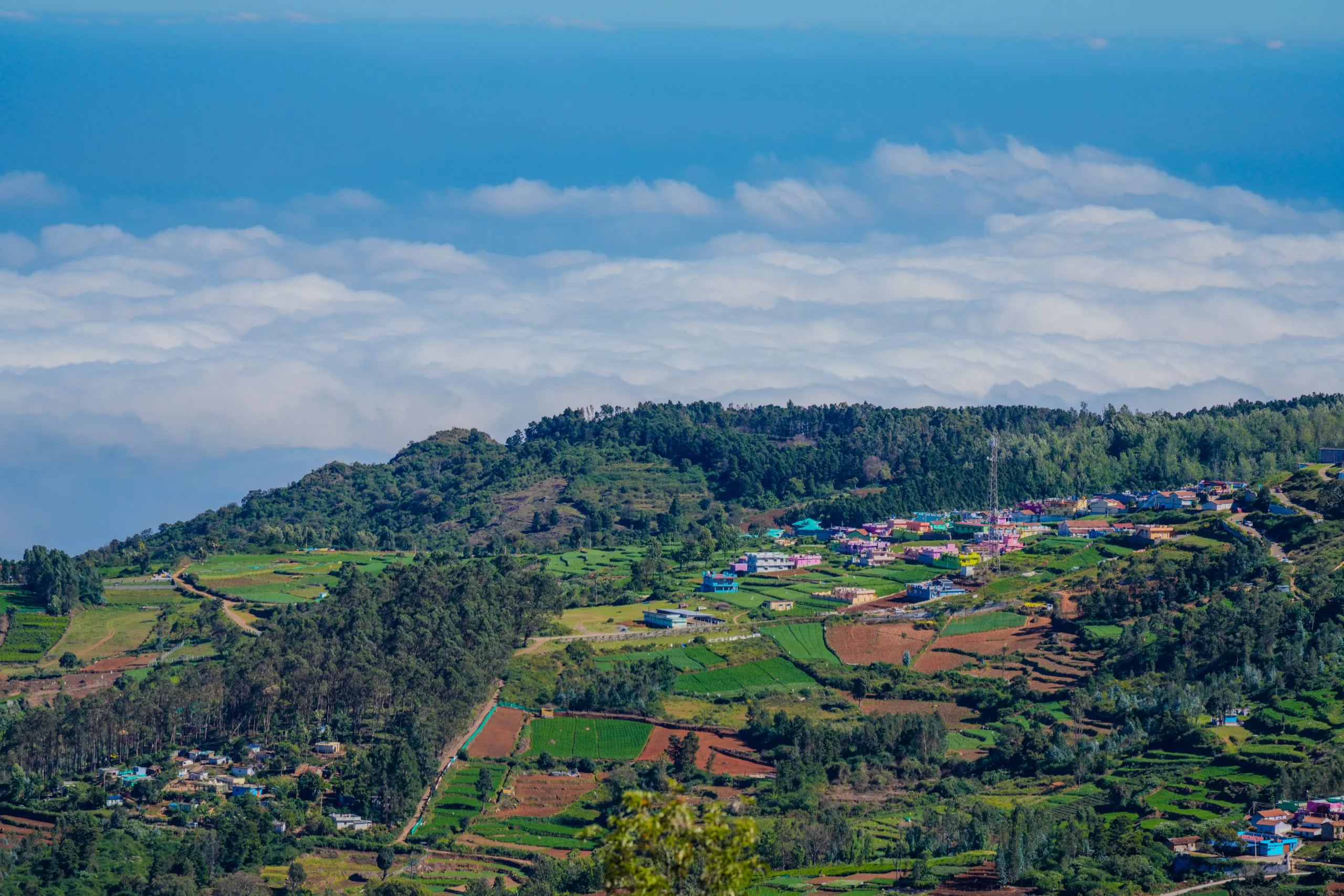 Colorful village in Ooty surrounded by terraced fields and cloud-filled hill views
