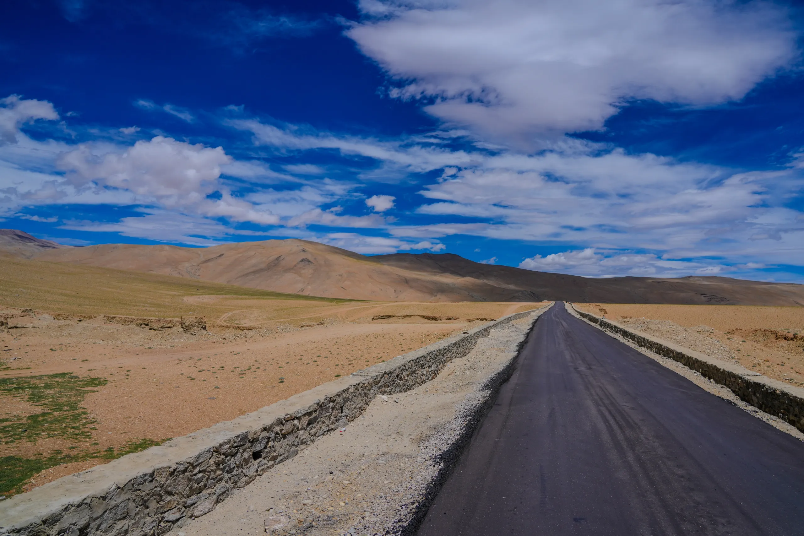 Straight blacktop road through a Leh desert valley under a deep blue sky