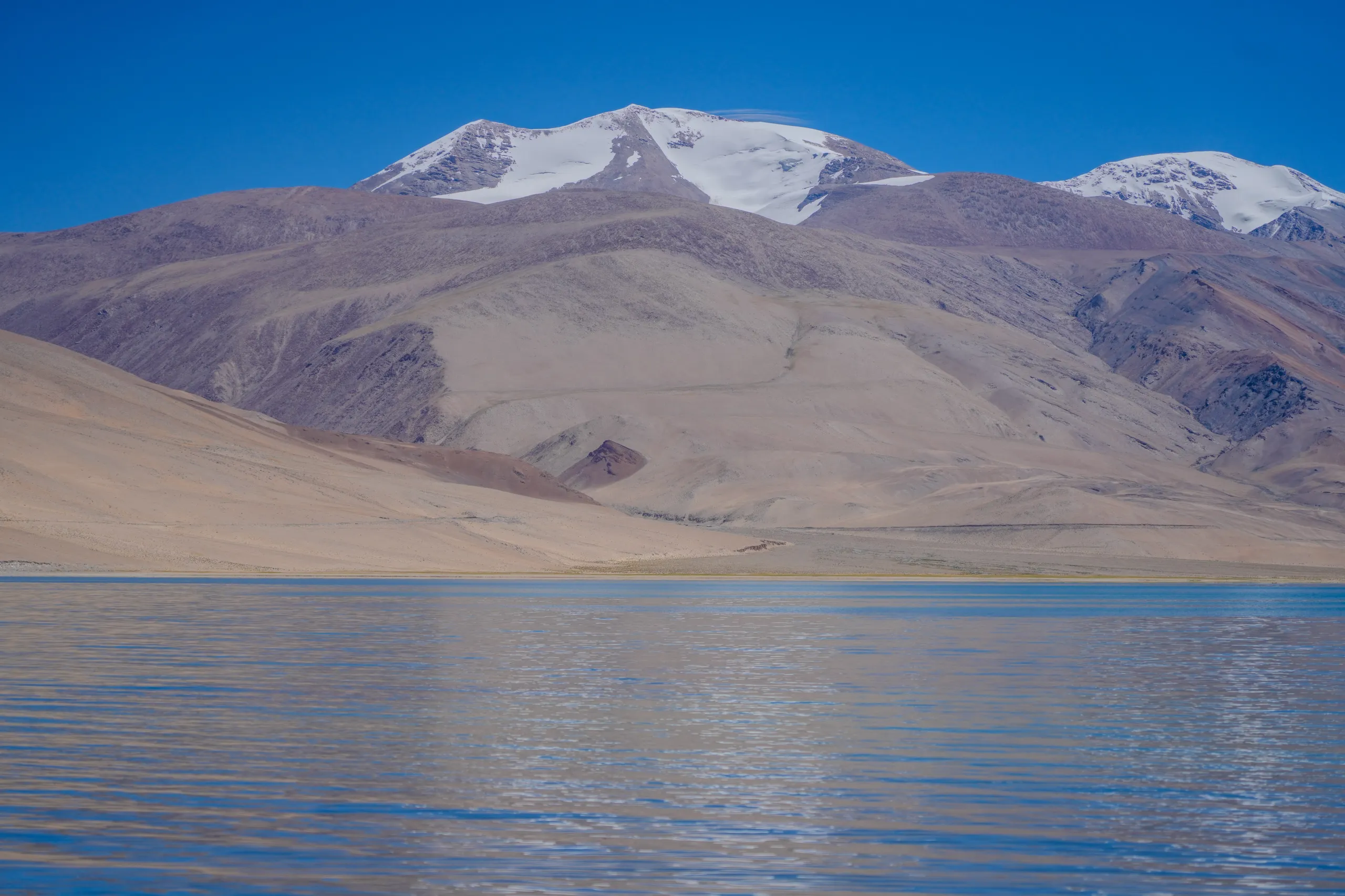 Snowy hillside reflected in the calm water of Tso Moriri Lake in Leh Ladakh
